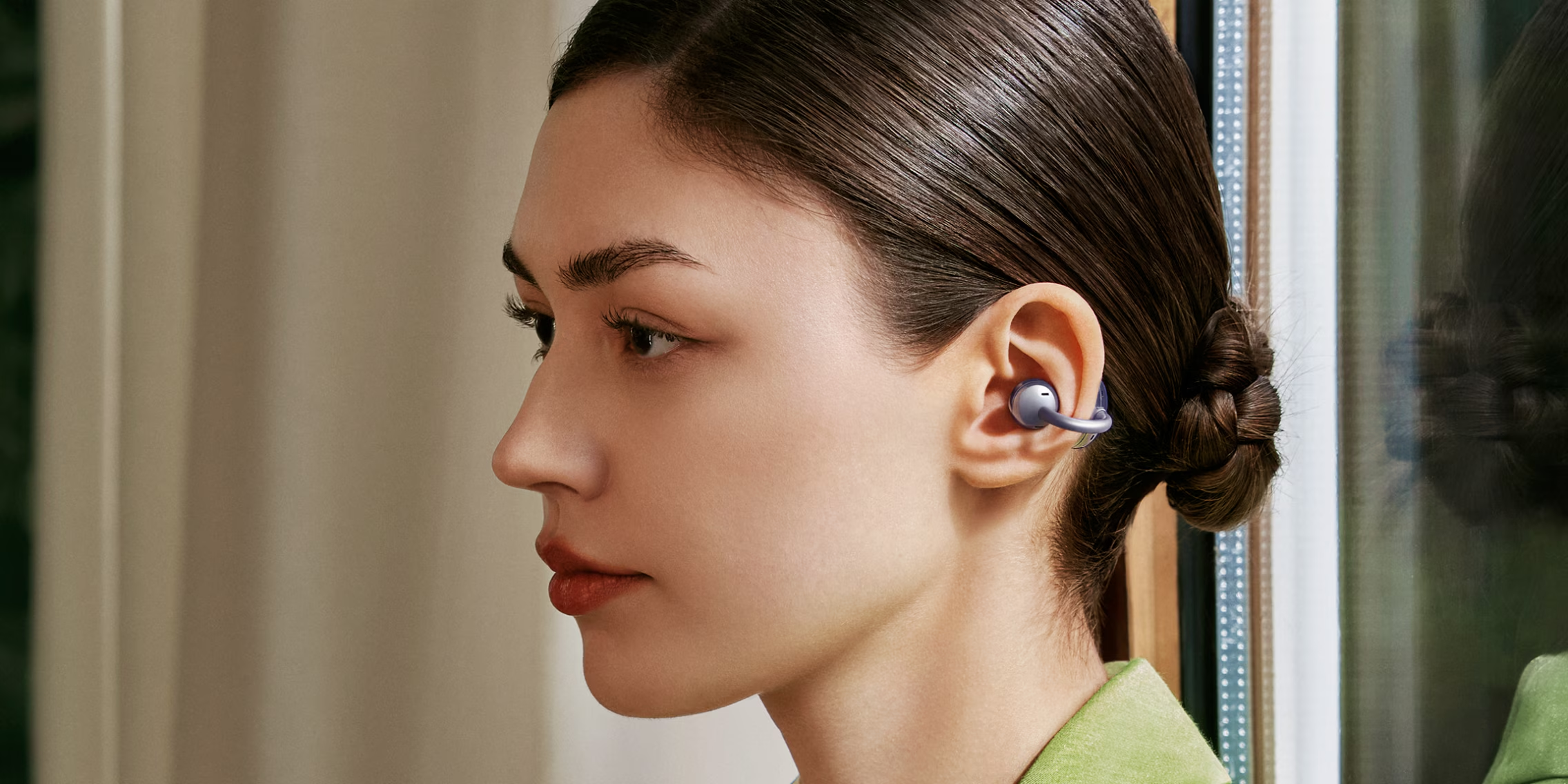 A woman wearing clip-on open-ear earbuds that resemble stylish ear cuff accessories.